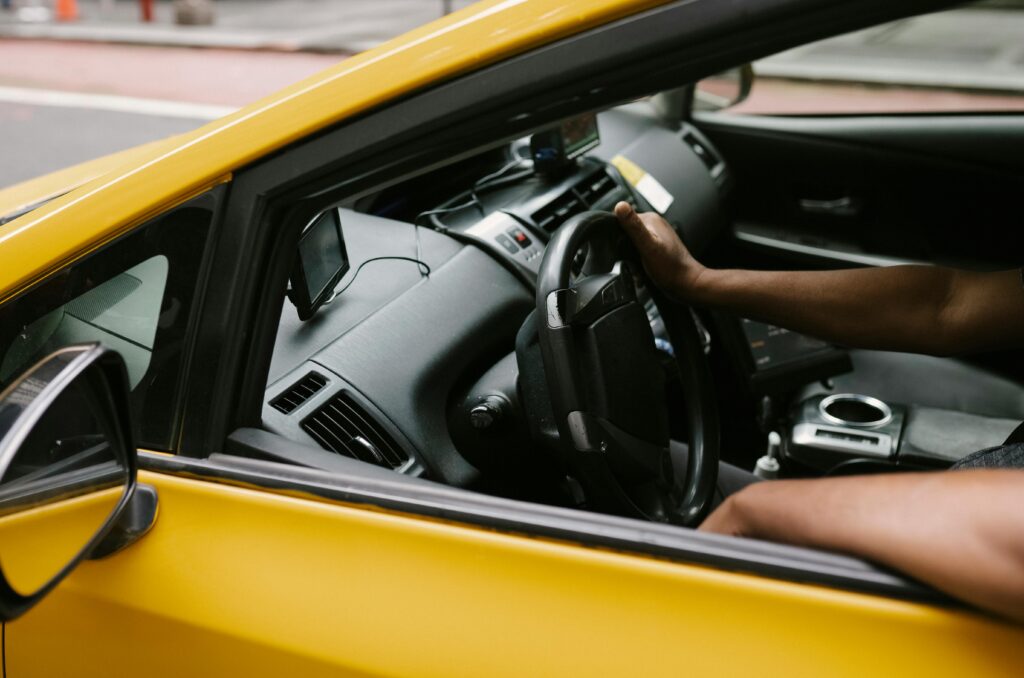 Close-up shot of a taxi driver steering a yellow cab on a city street.